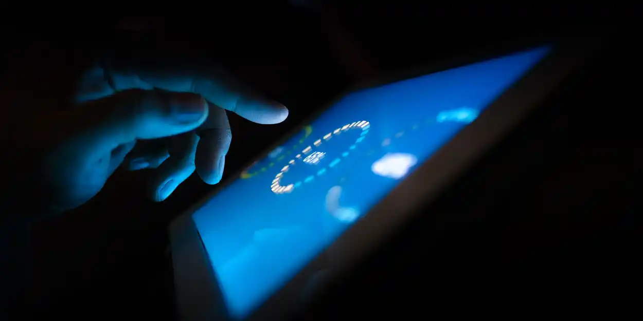 IES Dallas Section | Navigating the Time-Complexity Dilemma in Lighting Controls: Rethinking "Simplicity" | Hand touching a touch screen loading at 65% on a dark background